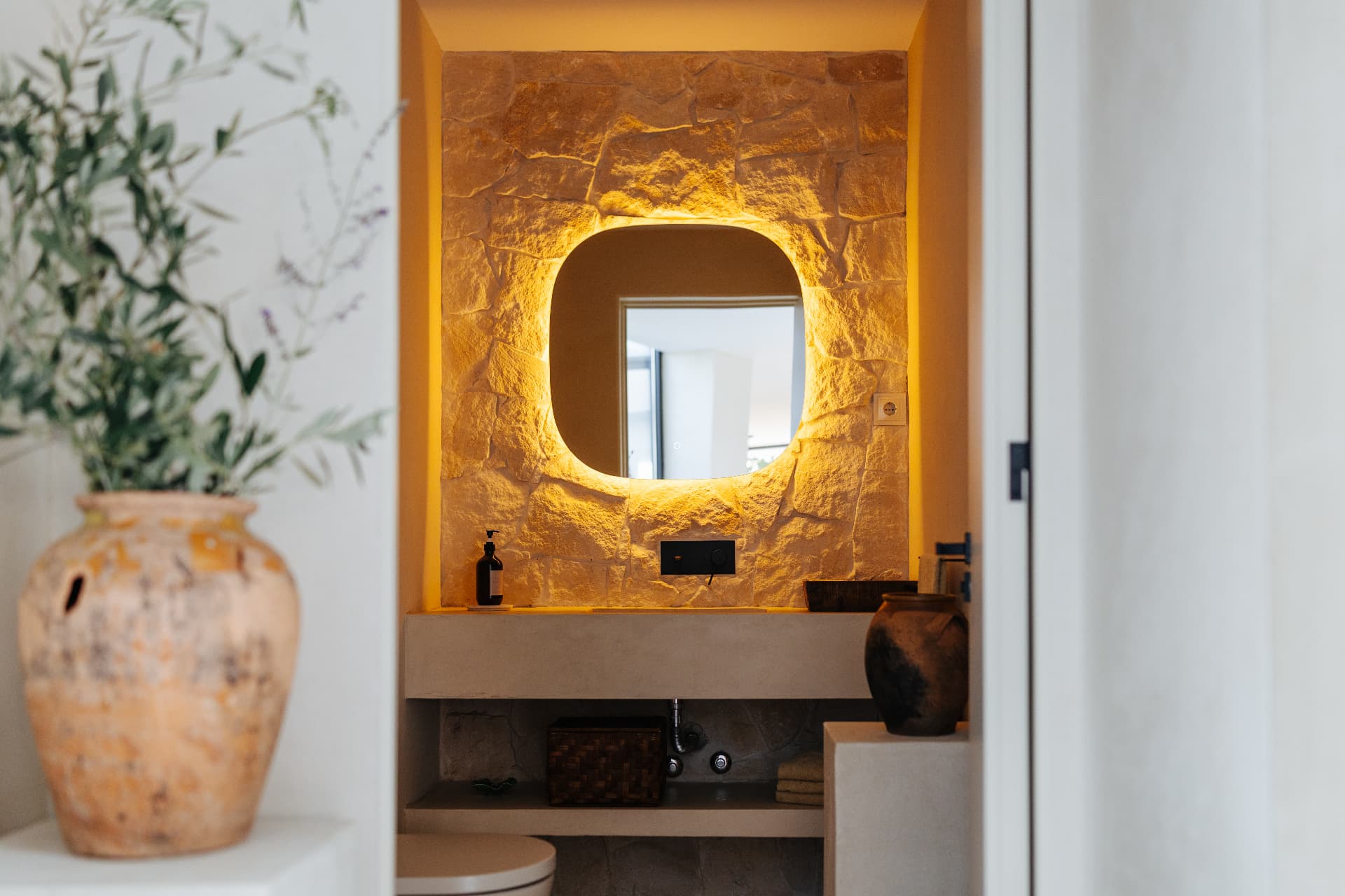 Bathroom with backlit mirror set into a natural stone wall