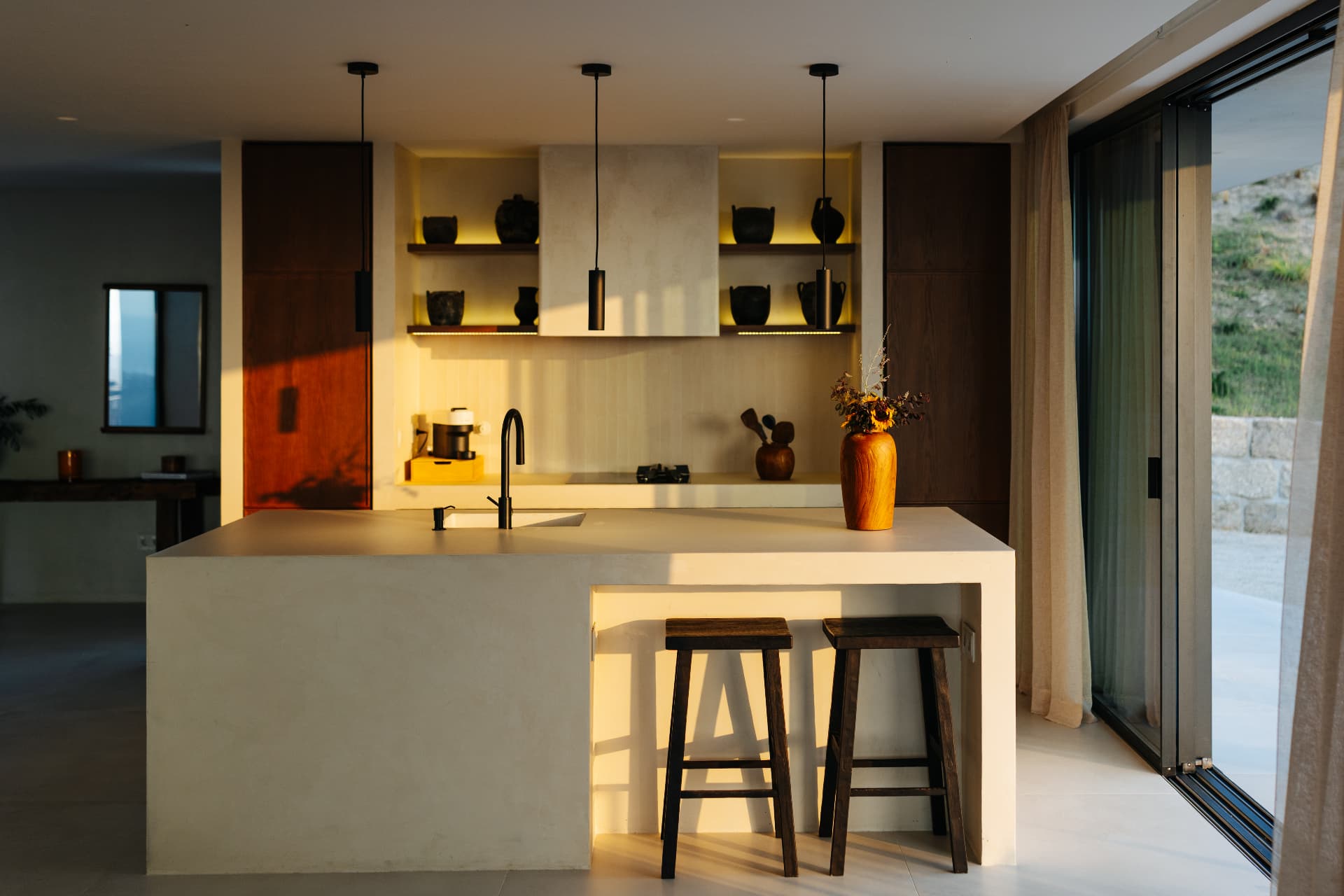 Microcement kitchen island with wooden stools in warm evening light
