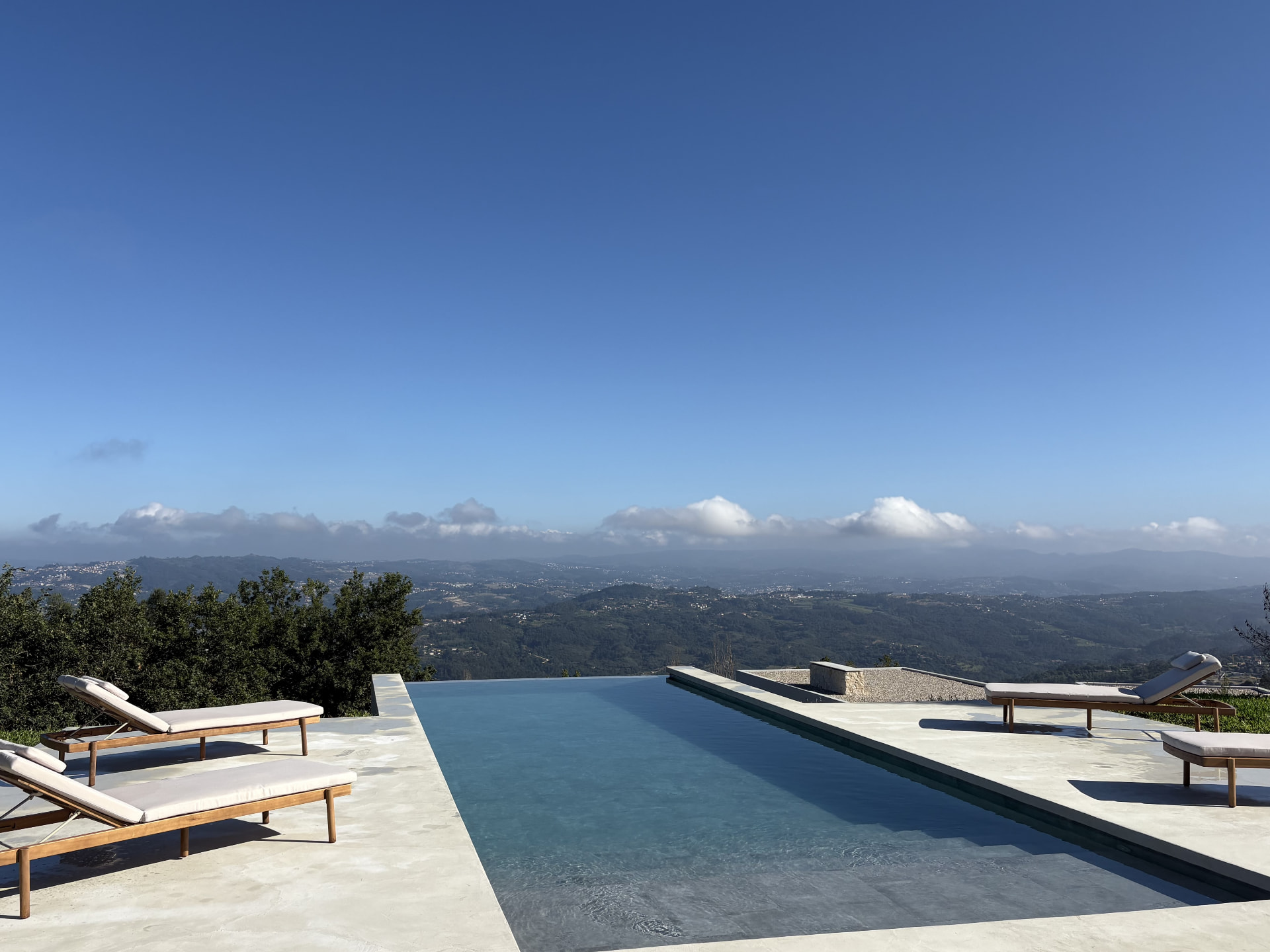 Infinity pool with wooden sun loungers overlooking the valley on a clear day