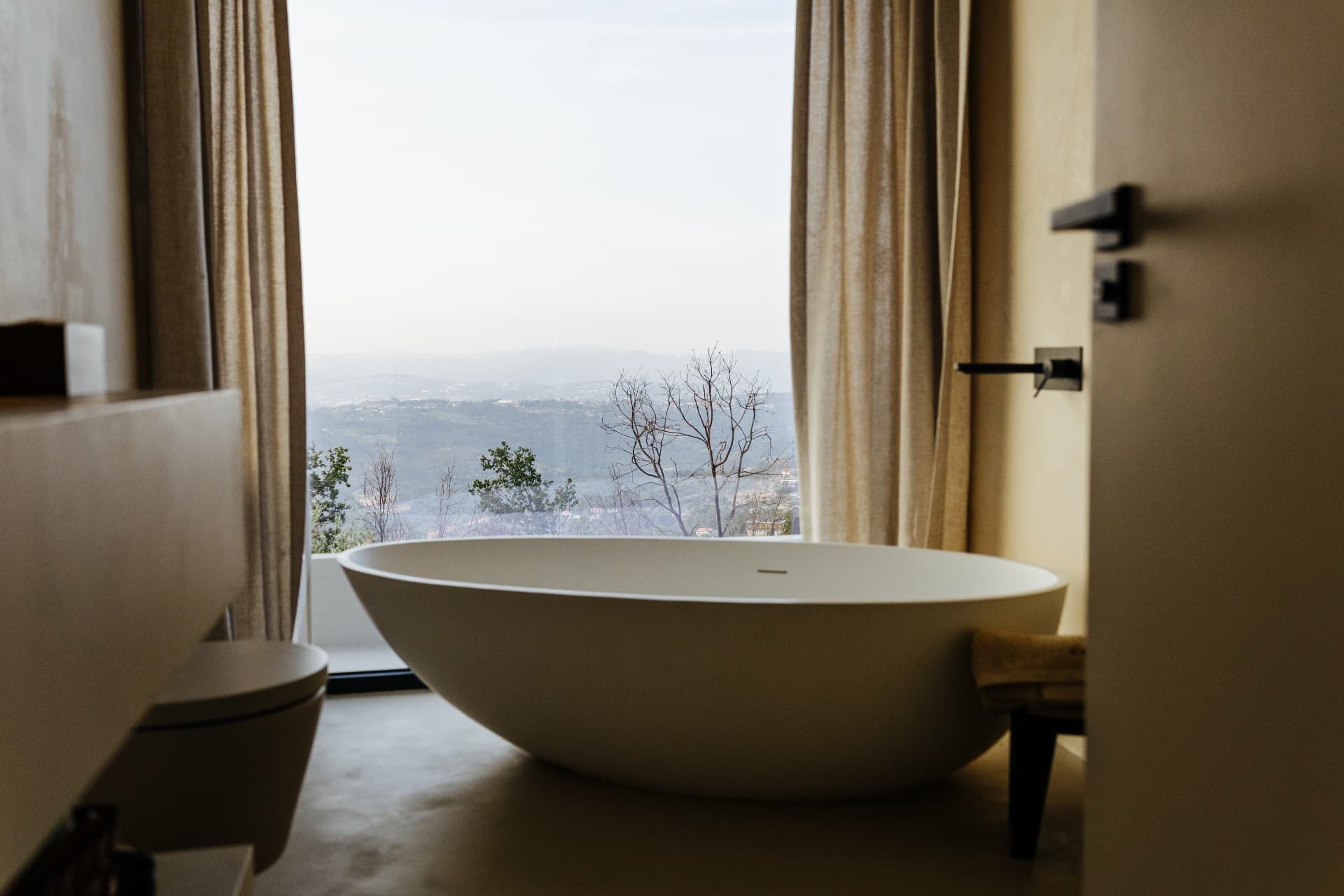 Freestanding bathtub facing a full-height window over the hills