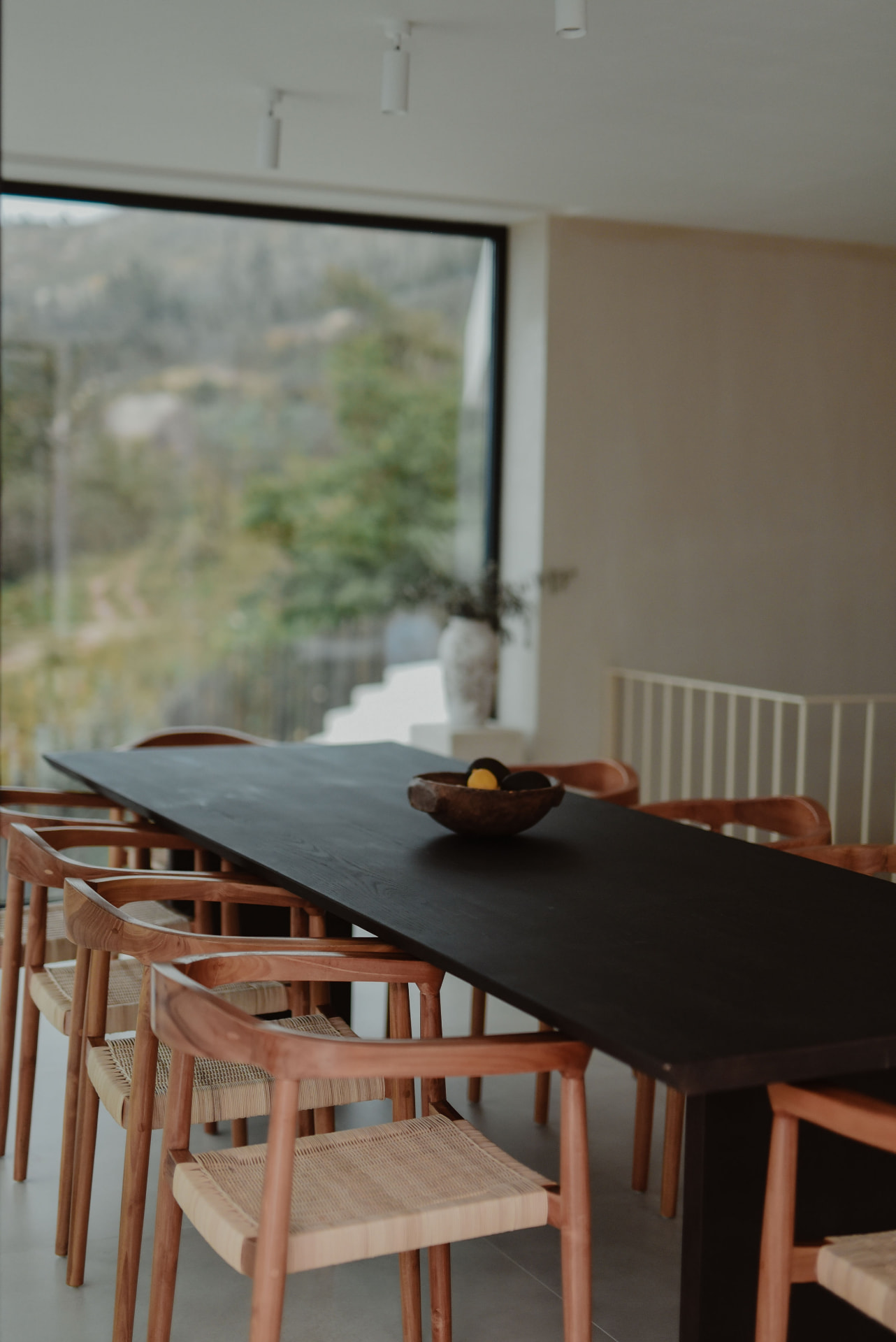 Long black dining table with wooden chairs and garden views