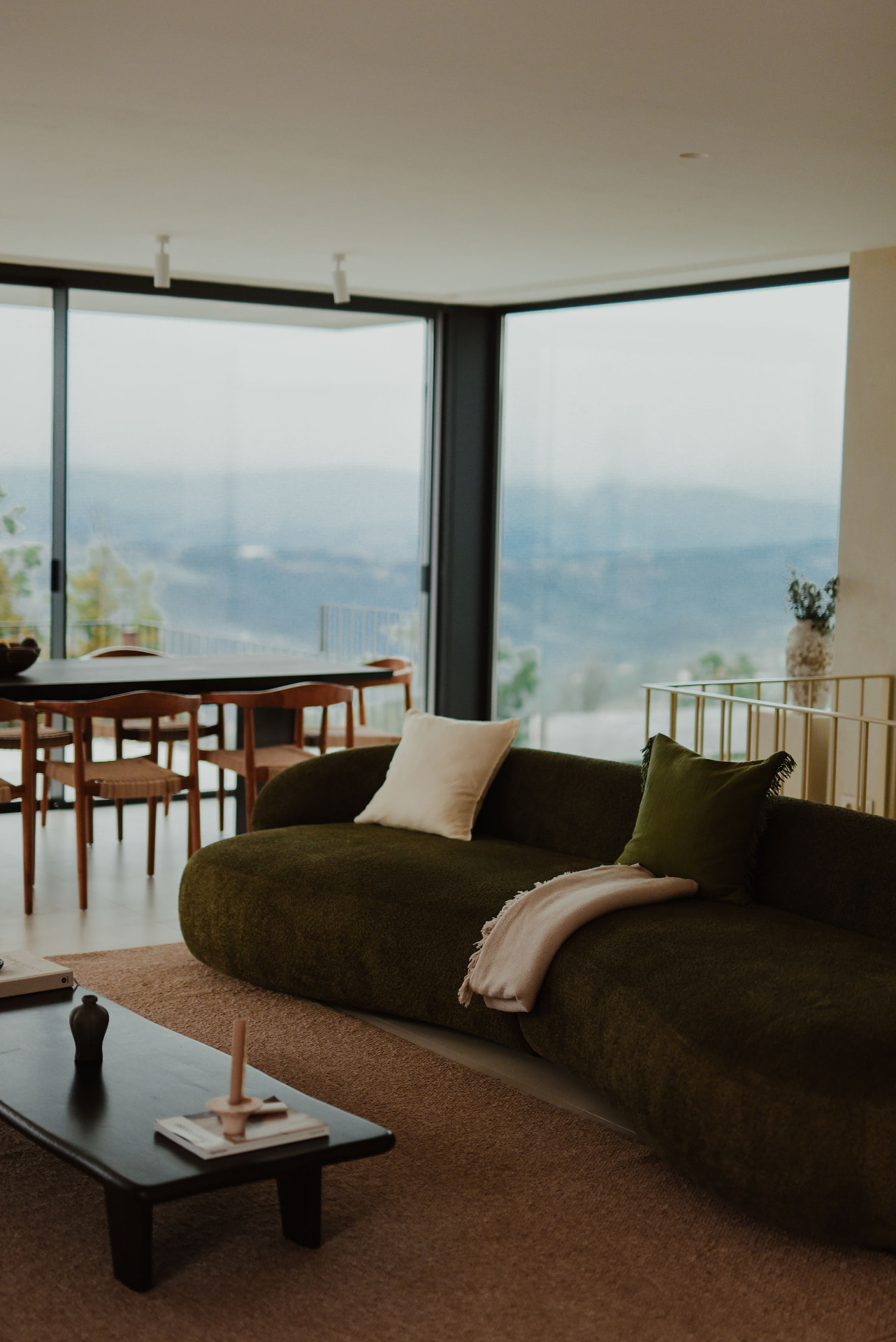 Open-plan living and dining space with a curved green sofa and valley views