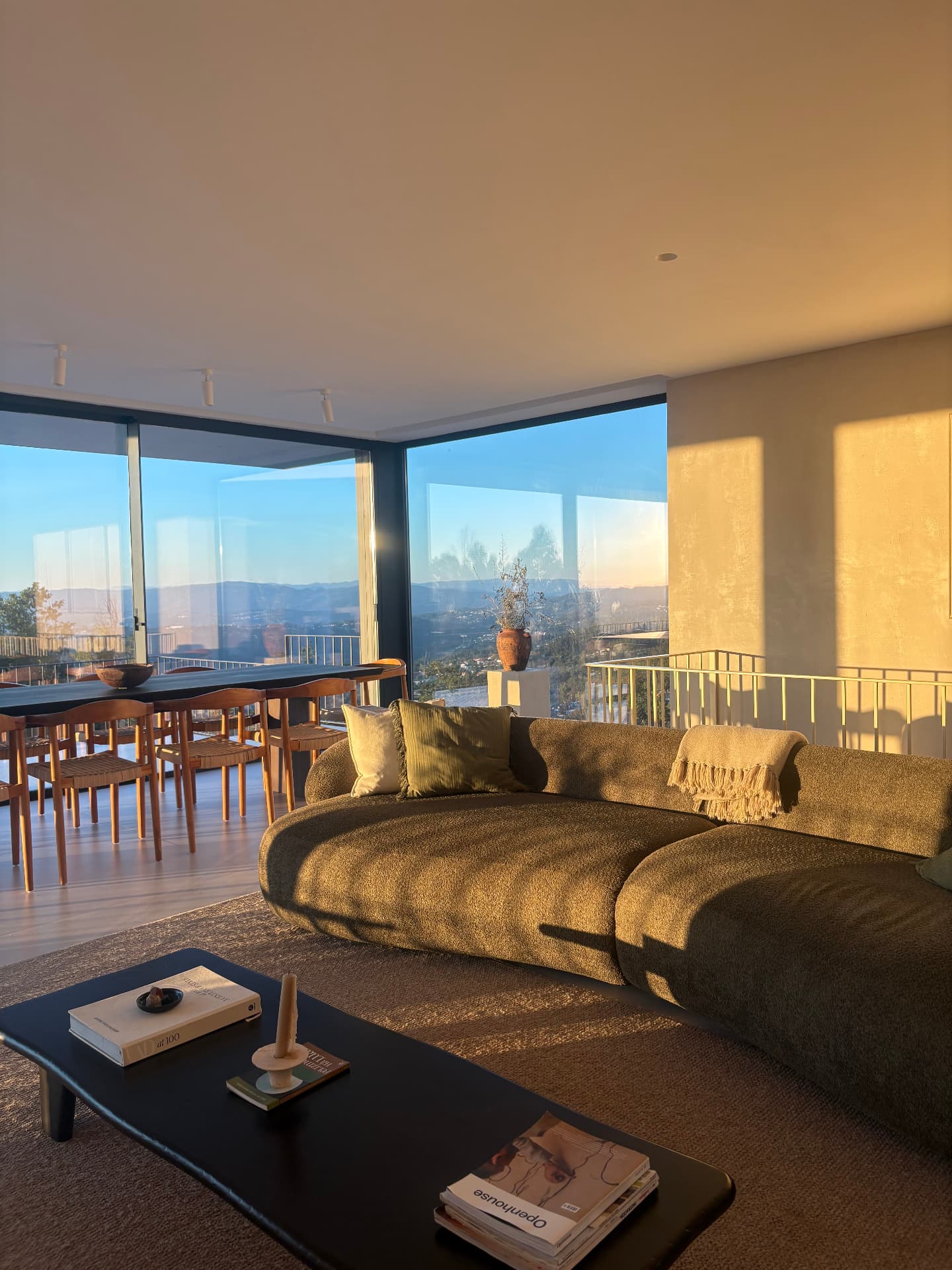 Curved green sofa and dining area filled with golden evening light and valley views