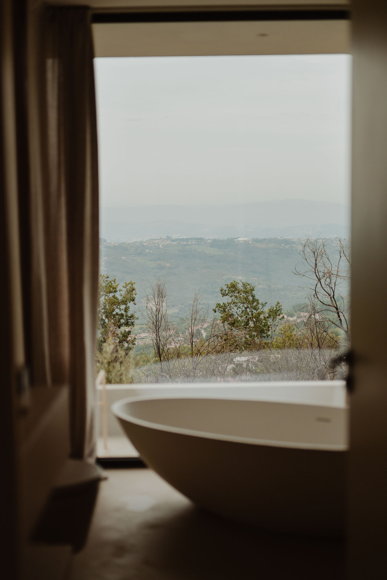 Freestanding bathtub framed by a window with misty valley views